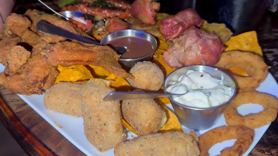 Bandeja de surtida Paulinos: pollo frito, chicharrón, chorizo, palitos de queso, patacones, aros de cebolla y dos salsas.